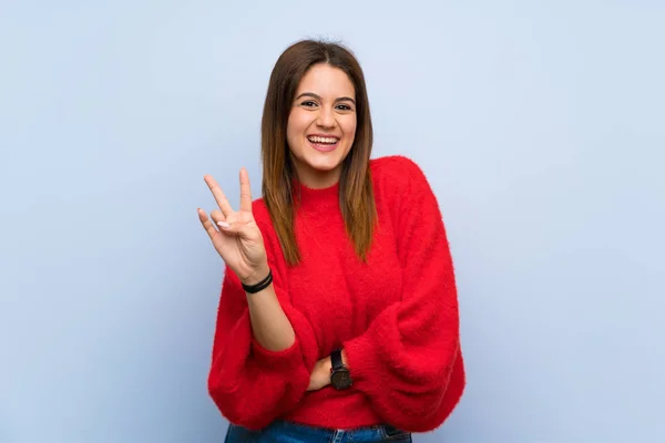 Young woman over isolated blue wall smiling and showing victory sign