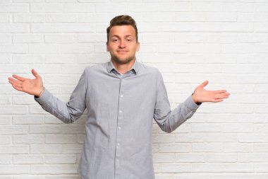 Ellerini kaldırırken şüpheleri olan beyaz tuğla duvar üzerinde Sarışın adam