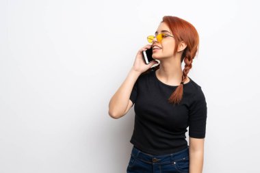 Beyaz duvarın ötesindeki genç kızıl kadın cep telefonuyla sohbet ediyor.