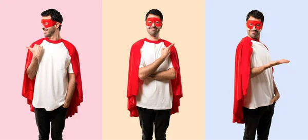 Set of Superhero man with mask and red cape pointing to the side with a finger to present a product or an idea while looking forward smiling on colorful background