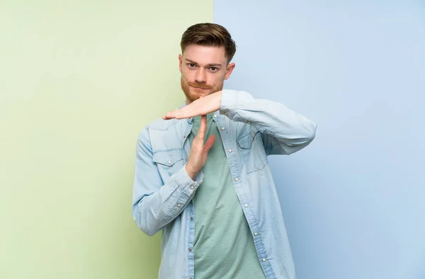 Redhead man over colorful background making time out gesture