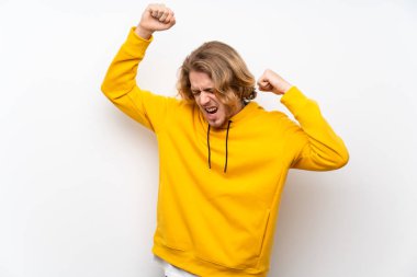 Beyaz duvar üzerinde sweatshirt ile Sarışın adam bir zafer kutluyor