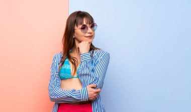 Bikinili genç bir kadın eli çenesinde yan tarafa bakıyor.