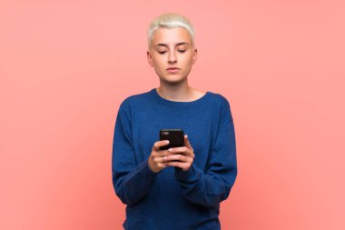 Pembe duvar üzerinde beyaz kısa saçlı genç kız cep ile bir mesaj gönderme