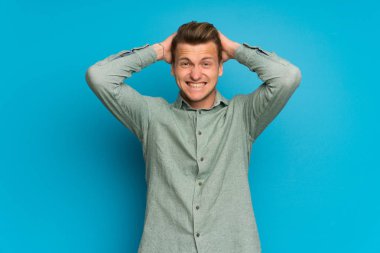 Izole mavi duvar üzerinde Sarışın adam sinirli ve baş elleri alır