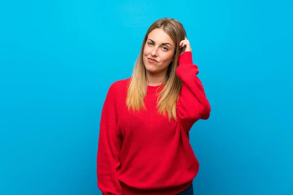 Woman with red sweater over blue wall having doubts