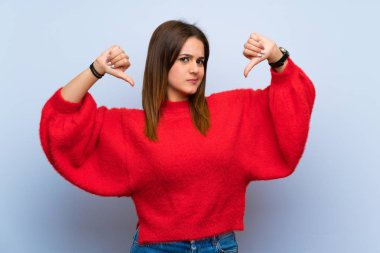 İzole edilmiş mavi duvarda baş parmağını gösteren genç bir kadın.