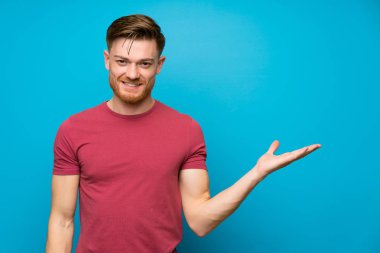 İzole mavi duvarda kızıl saçlı adam avuç içinde hayali copyspace tutan