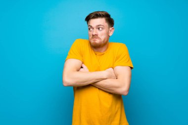 Omuzları kaldırırken mavi duvar üzerinde Redhead adam şüpheler jest yapıyor