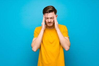 Baş ağrısı ile mavi duvar üzerinde Redhead adam