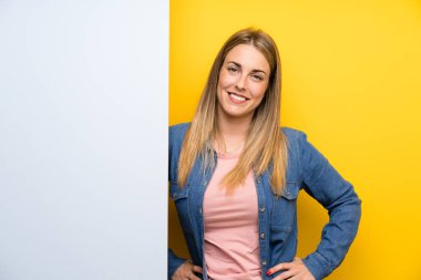 Kalçasında kollarıyla poz veren boş bir pankart tutan genç kadın.