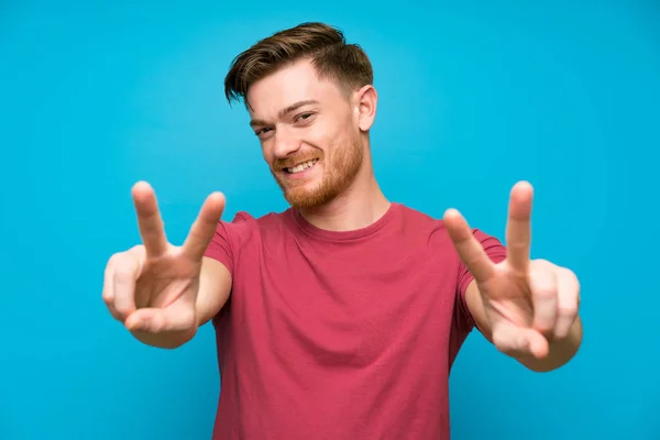 Redhead Muž Izolované Modré Stěně Usmívá Zobrazuje Vítězné Znamení — Stock fotografie