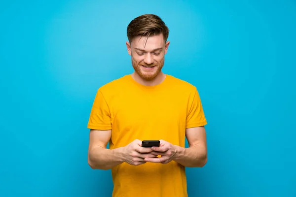 Ruda Mężczyzna Nad Niebieską Ścianą Wysyłając Wiadomość Telefonem — Zdjęcie stockowe