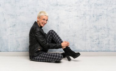 Genç kadın kollarını kavuşturup yerde oturuyor ve ileriye bakıyor.