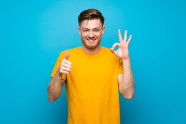 Mavi duvar üzerinde Redhead adam ok işareti ve başparmak yukarı jest gösteren