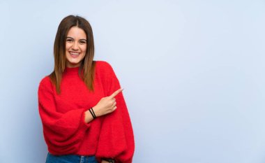 Bir ürün sunmak için yan işaret izole mavi duvar üzerinde genç kadın