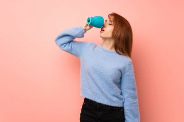 Bir fincan sıcak kahve elinde pembe bir arka plan üzerinde genç Kızıl saçlı kadın