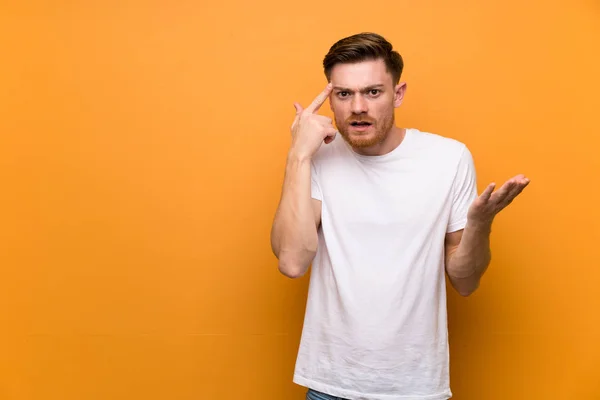 Redhead man over brown wall making the gesture of madness putting finger on the head