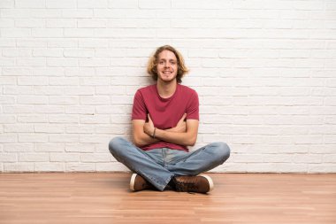 Sarışın adam kollarını ön pozisyonda geçti tutarak yerde oturan