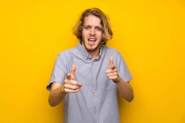 Sarışın adam izole sarı arka plan üzerinde ön işaret ve gülümseyen