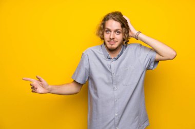 Izole sarı arka plan üzerinde Blonde adam şaşırttı ve yan parmak işaret