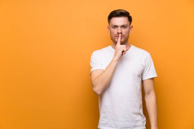 Kahverengi duvarın üzerinde kızıl saçlı adam ağzına parmak koyarak sessizlik jest bir işareti gösteren