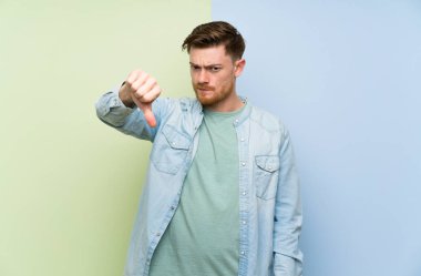 Renkli arka plan üzerinde Redhead adam olumsuz ifade ile başparmak aşağı gösteren