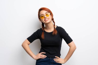 Silah, kalça ile poz ve gülümseyen beyaz duvar genç Kızıl saçlı kadın