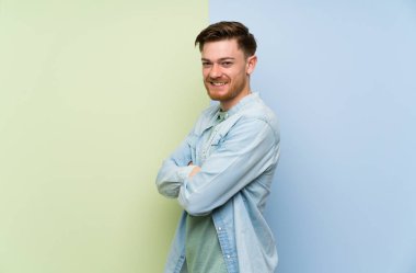 Kolları geçti ve ileriye bakan renkli arka plan üzerinde Redhead adam