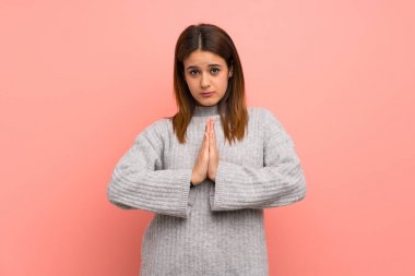 Pembe duvarın üzerindeki genç kadın avuç içlerini bir arada tutuyor. İnsan bir şey ister.