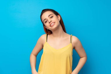 Genç kızıl saçlı kadın mavi arka planda gülüyor.