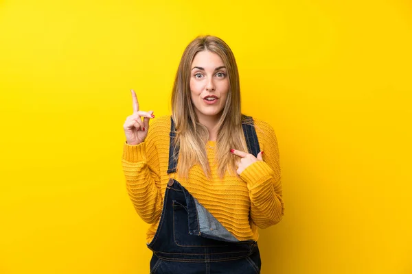 Vrouw Met Overalls Geïsoleerde Gele Muur Met Verrassende Gezichtsuitdrukking — Stockfoto