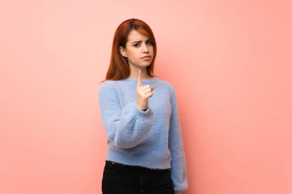 Young redhead woman over pink background serious and pointing to the front