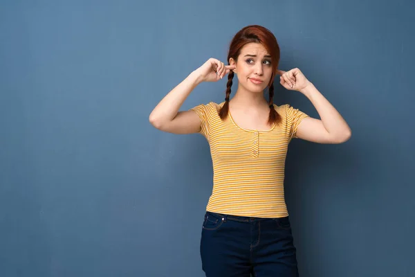 Joven Pelirroja Sobre Fondo Azul Cubriendo Ambas Orejas Con Las —  Fotos de Stock