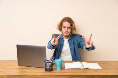 Bir laptop gülümseyen ve zafer işareti gösteren sarışın adam