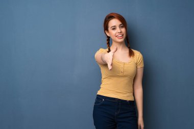 Mavi arka plan iyi bir anlaşma kapanış için el sıkışan genç Kızıl saçlı kadın