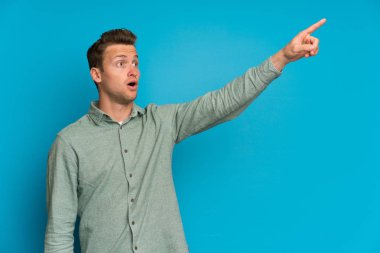 İzole mavi duvar üzerinde sarışın adam uzağa işaret