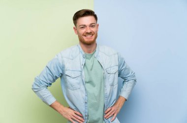 Renkli arka plan üzerinde Redhead adam kalça kolları ile poz ve gülümseyerek