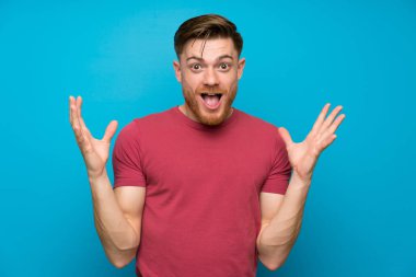 Sürpriz yüz ifadesi ile izole mavi duvarda Redhead adam