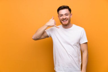 Kahverengi duvarın üstündetelefon hareketi yapan kızıl saçlı adam. Beni geri arayın işareti