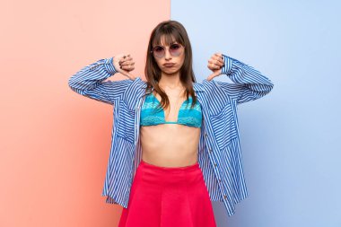 Bikinili genç bir kadın iki eliyle baş parmağını aşağı gösteriyor.