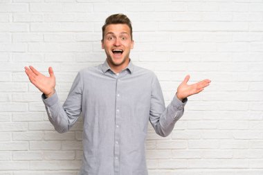 Şok yüz ifadesi ile beyaz tuğla duvar üzerinde Blonde adam