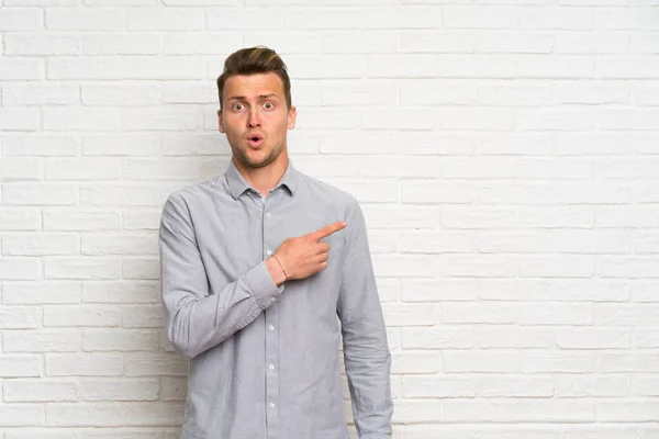 Blonder Mann Über Weiße Backsteinmauer Überrascht Und Zeigt Seite — Stockfoto