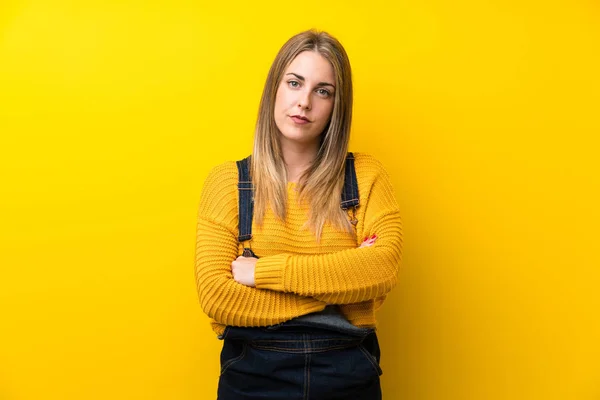 Mujer Con Overoles Sobre Pared Amarilla Aislada Manteniendo Los Brazos —  Fotos de Stock