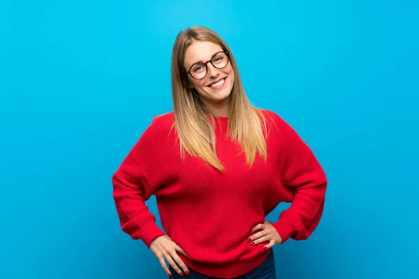 Woman with red sweater over blue wall with glasses and smiling