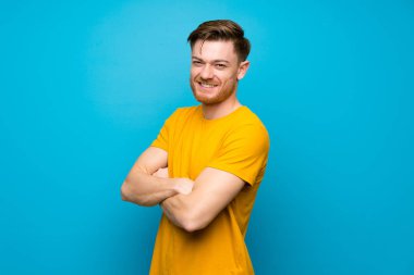Kolları çapraz ve ileriye bakan mavi duvar üzerinde Redhead adam