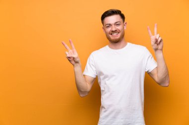 Kahverengi duvarın üzerinde iki eliyle zafer işareti gösteren kızıl saçlı adam