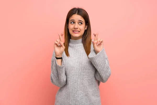 Young woman over pink wall with fingers crossing and wishing the best