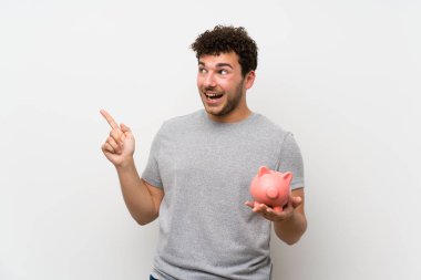 Büyük bir kumbara tutan izole duvar üzerinde kıvırcık saçlı adam