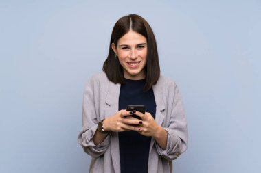 Young woman over isolated blue wall sending a message with the mobile